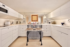 A modern kitchen with white cabinetry, a central island with a checkered tablecloth, and a microwave above the counter. - Place Vendôme – A stylish and elegant apartment (Paris)