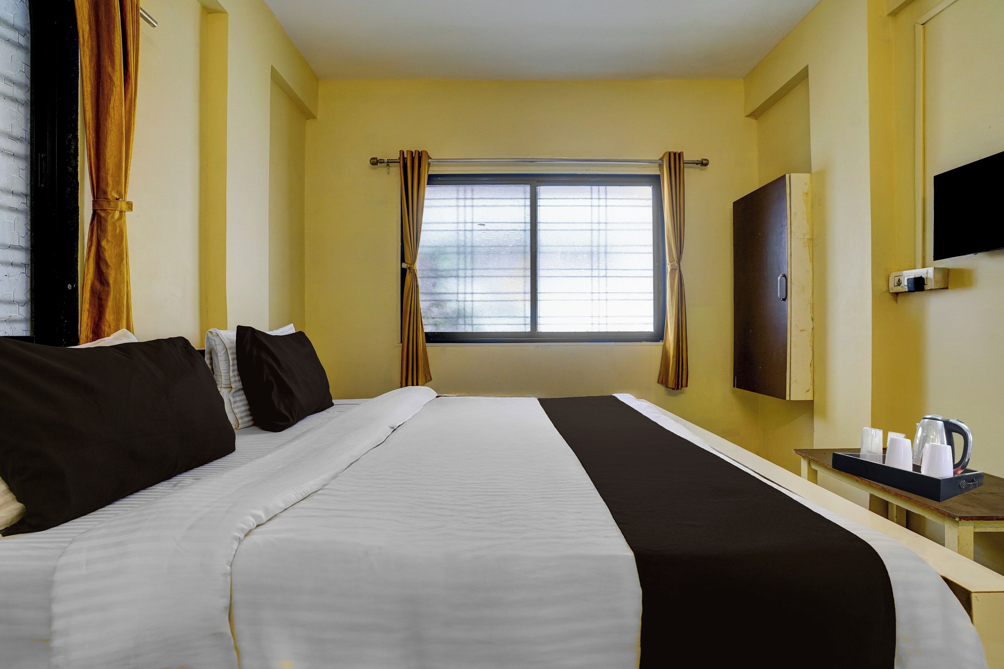 Habitación de hotel con cama, escritorio con hervidor y tazas, ventana con cortinas y televisor de pantalla plana en la pared.