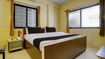 Una habitación de hotel con cama, mesita de noche, un florero y una ventana con cortinas.