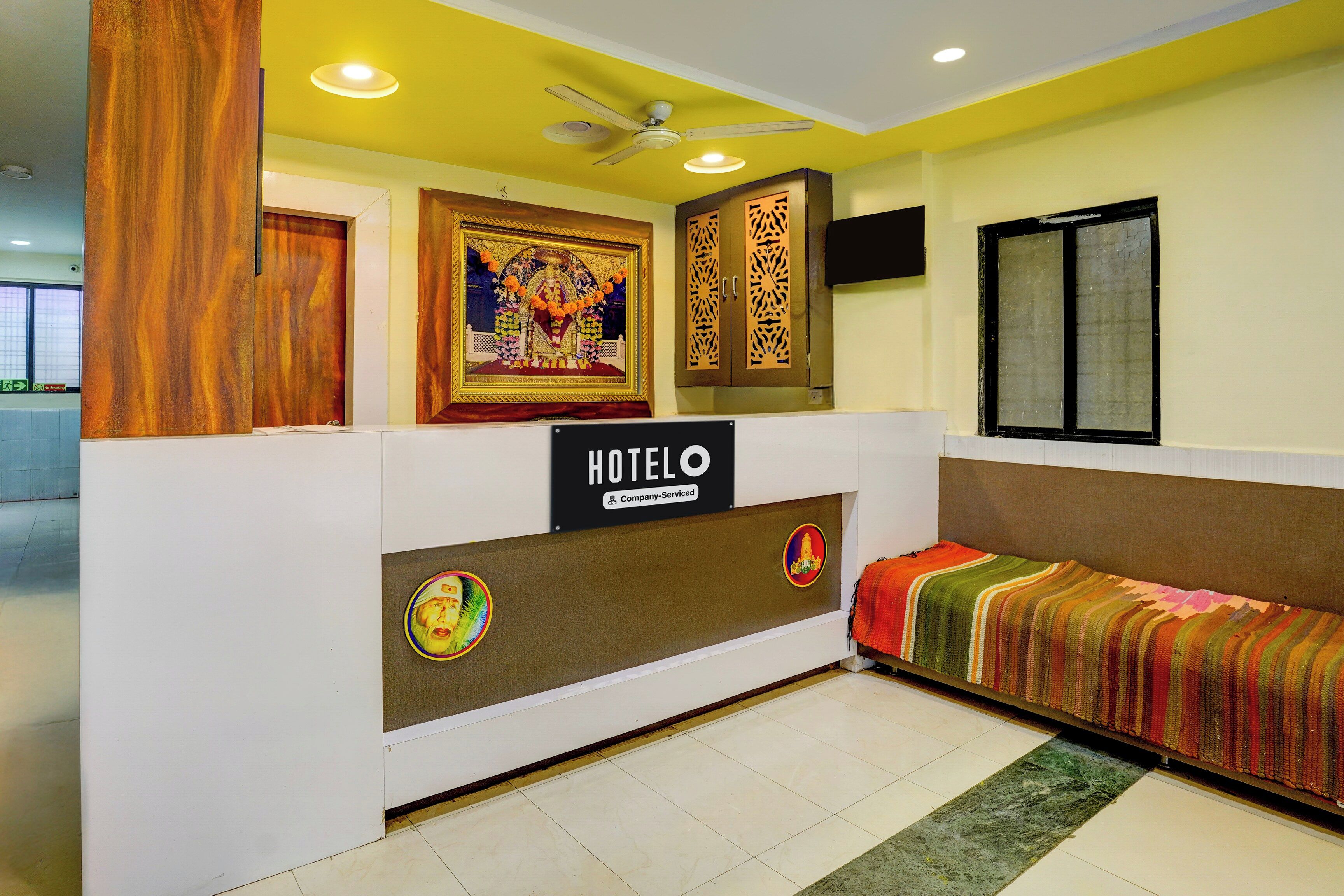 Zona de recepción de hotel con mostrador, señal que indica que el hotel cuenta con servicios para empresas, y una cama con una colcha colorida.
