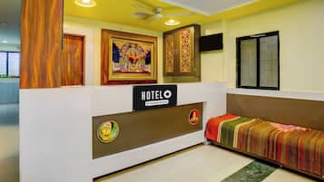 Zona de recepción de hotel con mostrador, señal que indica que el hotel cuenta con servicios para empresas, y una cama con una colcha colorida.