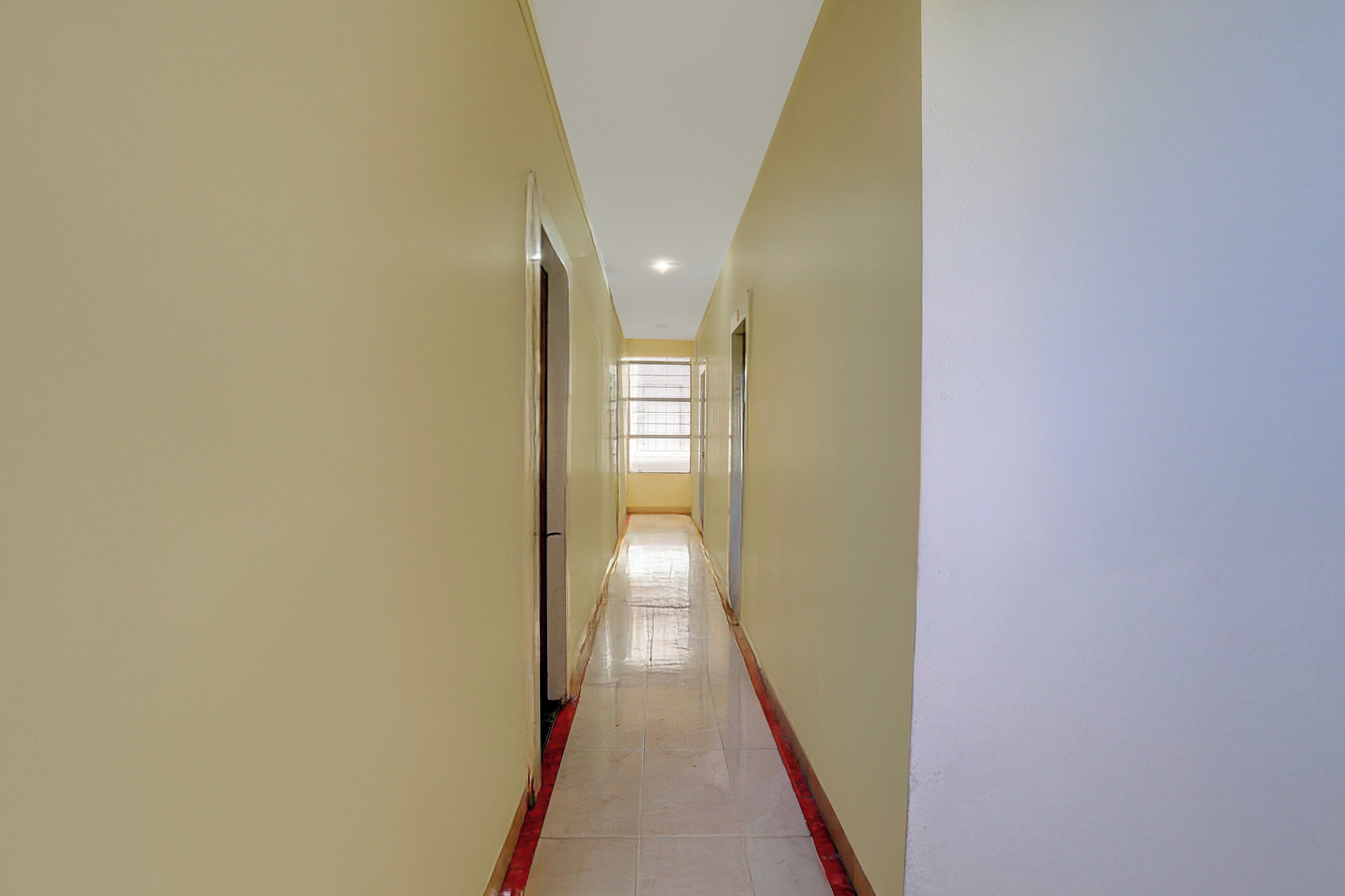 A long, narrow hallway with a tiled floor and a red border at the bottom.
