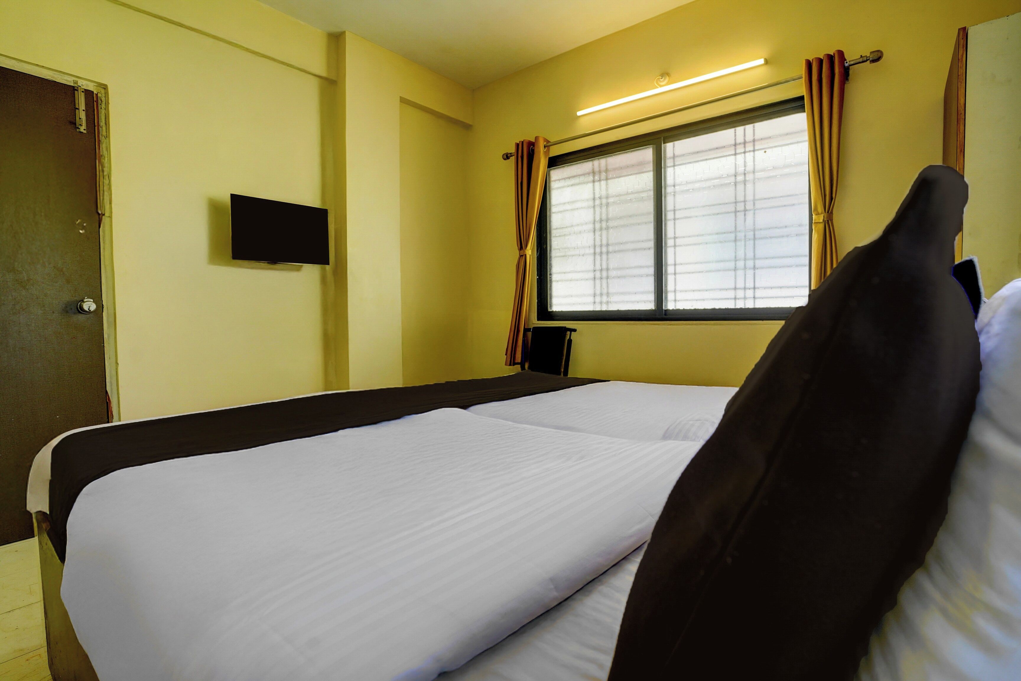 A hotel room with a bed, a television on the wall, and a window with curtains.