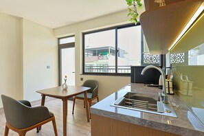 A modern kitchen with a built-in sink, a dining area with a table and chairs, and a large window offering a view of the outside. - D&D Apartment & Hotel (Ngo thi sy)