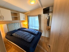 A compact bedroom with a bed, bedside lamps, a TV, and a window with curtains. - Klein Vink Vacation Park - Boulevard 36 (Arcen)