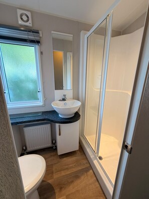 A compact bathroom with a toilet, a sink, a mirror, and a shower enclosure. - Klein Vink Vacation Park - Boulevard 36 (Arcen)