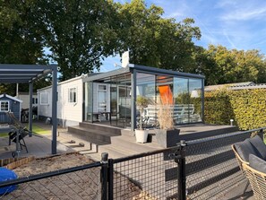 A modern, glass-enclosed building with a patio area, surrounded by a fence and trees. - Klein Vink Vacation Park - Boulevard 36 (Arcen)