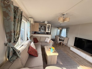 A compact living space with a sofa, a television, a dining area, and a kitchenette. - Klein Vink Vacation Park - Boulevard 36 (Arcen)