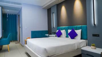 Habitació d'hotel moderna amb un llit gran, una tauleta de nit, una cadira i una taula petita amb una planta.