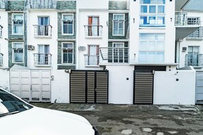 Kerrostalo, jossa on useita kerroksia, parvekkeita, portti ja valkoinen auto pysäköitynä sen eteen.