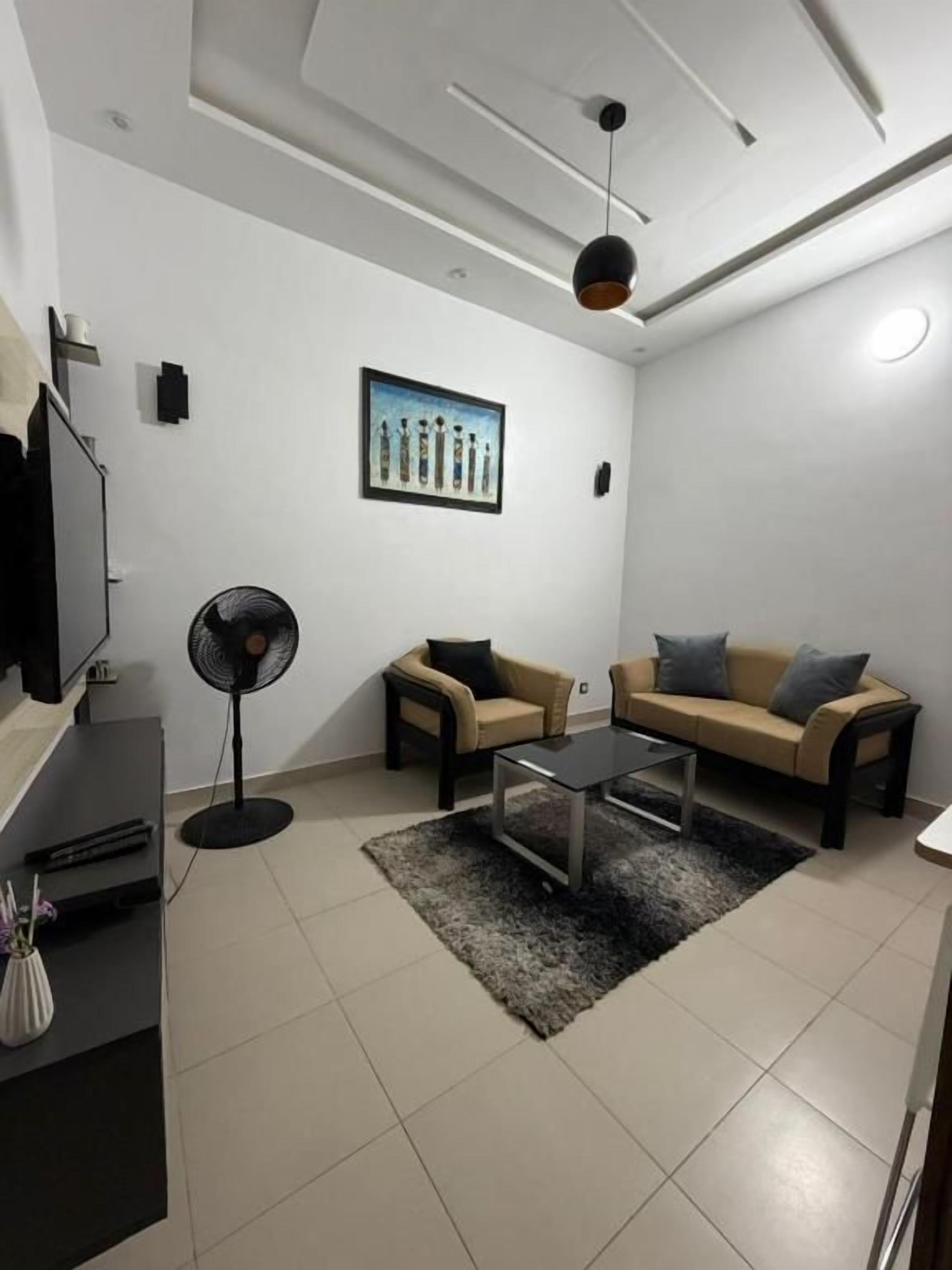 A modern living room with a sofa, a coffee table, a fan, and a painting on the wall.