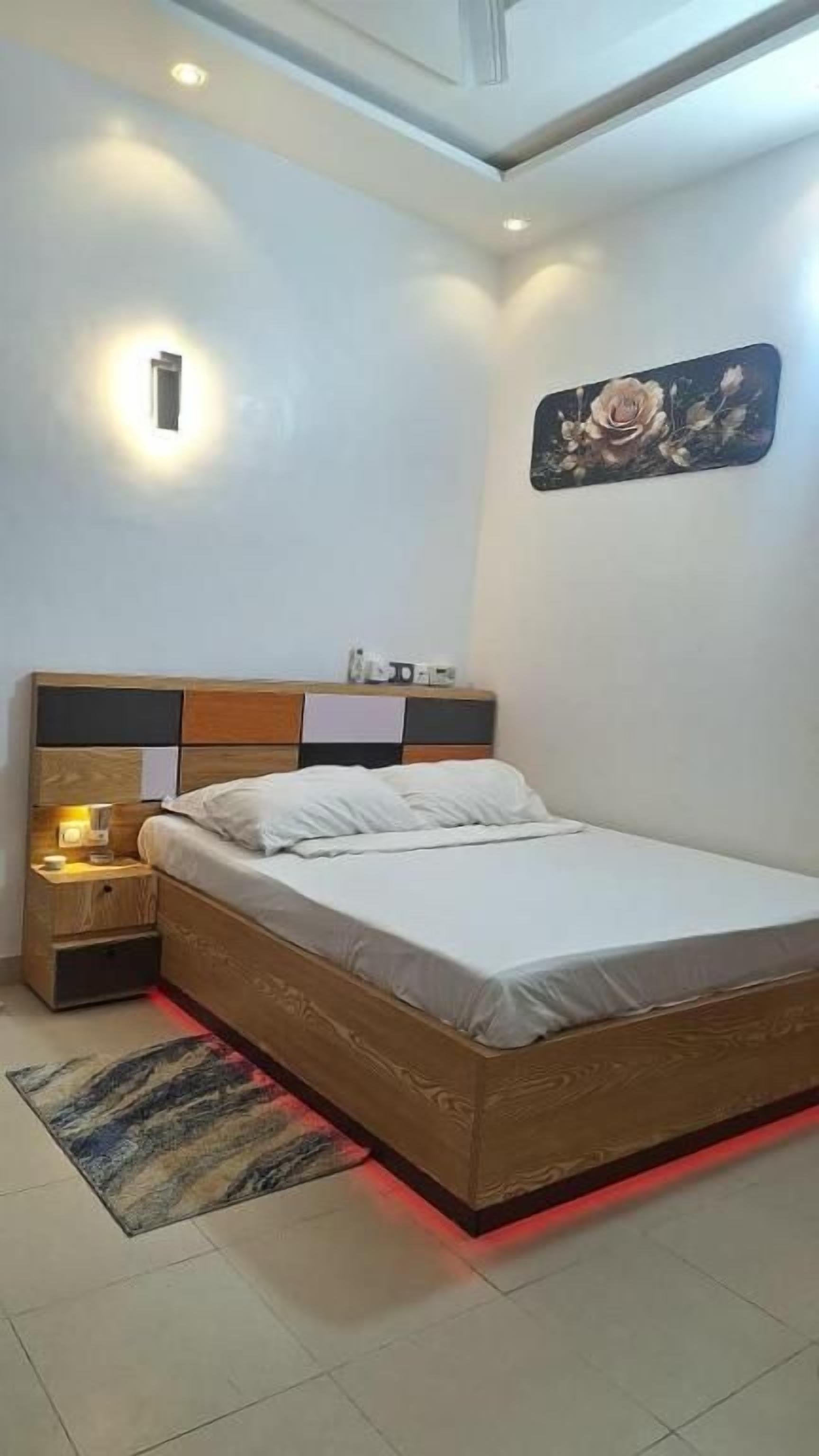 A bedroom with a bed, bedside table, wall-mounted light, and a rug.