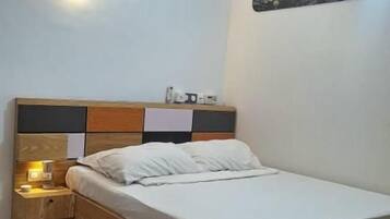 A bedroom with a bed, bedside table, wall-mounted light, and a rug.
