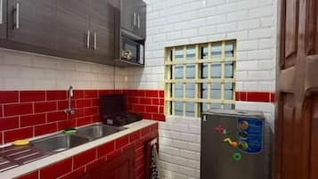 A kitchen with red and white tiled walls, a stainless steel sink, and a black refrigerator with energy efficiency stickers.