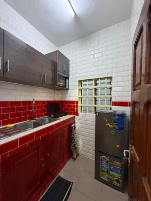 A kitchen with red and white tiled walls, a stainless steel sink, and a black refrigerator with energy efficiency stickers.
