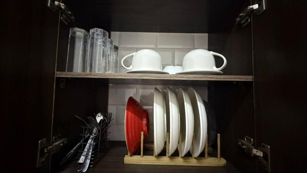 Une cuisine avec des étagères où sont rangées des tasses, des assiettes et un égouttoir rouge.