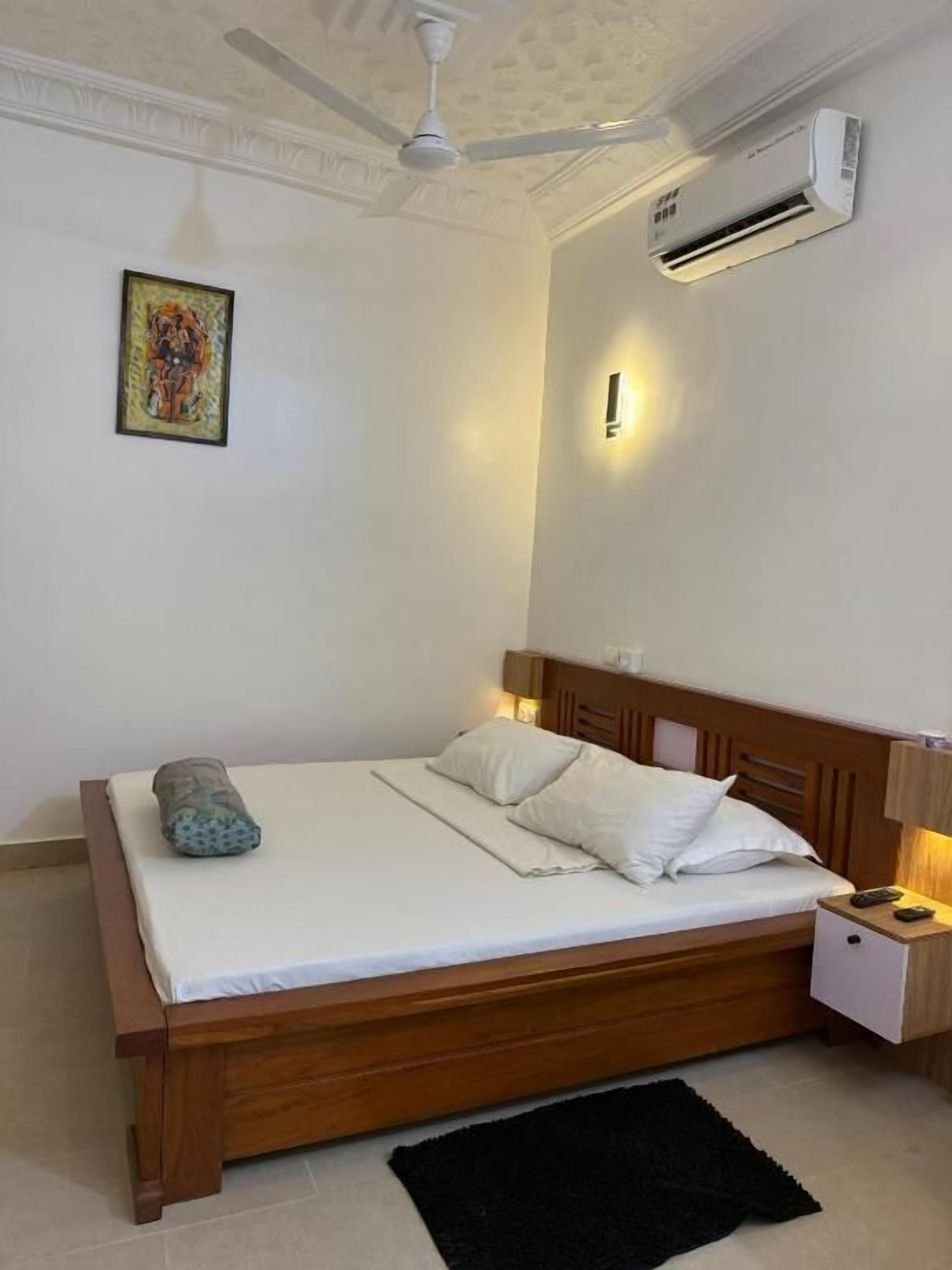 Une chambre à coucher avec un lit en bois, une table de chevet, un climatiseur fixé au mur et un ventilateur de plafond.