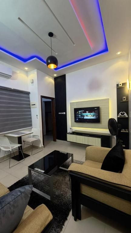 Una sala de estar moderna con televisor de pantalla plana, sofá, mesa de centro e iluminación colgante.