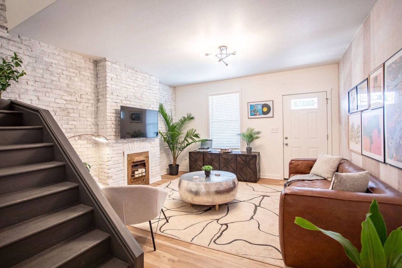 Ein Wohnzimmer mit Kamin, einem an der Wand montierten Fernseher, einem braunen Ledersofa und einer Treppe.