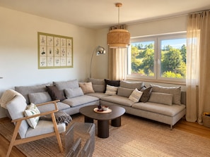 A modern living room with a sectional sofa, a round coffee table, and a hanging light fixture. - Modern, kid-friendly, surrounded by nature: Vacation home for 8 in the Southern Eifel (Bitburg)