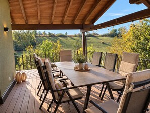Eine Terrasse im Freien mit einem Holztisch und -stühlen, umgeben von einem Metallgeländer, mit Blick auf eine hügelige Landschaft.