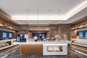 Een moderne hotellobby met een centraal gelegen receptiebalie, een zithoek en een koffiehoek.