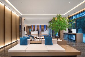Een moderne lobby met een zithoek, een koffiebar en een groot raam met uitzicht op het omliggende landschap.