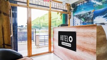 Una recepción de hotel con un letrero 'HOTELO', vista al exterior y un ventanal con vista a una montaña.