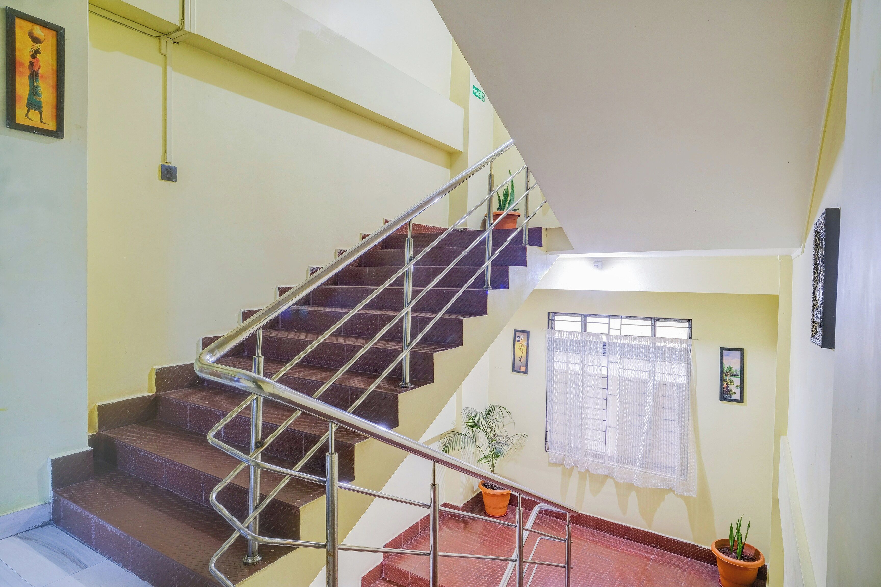 Uma escadaria com corrimão de metal, um vaso de planta e uma janela com cortinas.