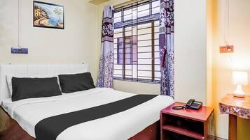 Habitación de hotel con una cama, una mesita de noche con teléfono, una lámpara de pared y una ventana con cortinas estampadas.