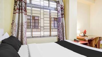 Una habitación de hotel con una cama, un escritorio con lámpara y una ventana con cortinas.