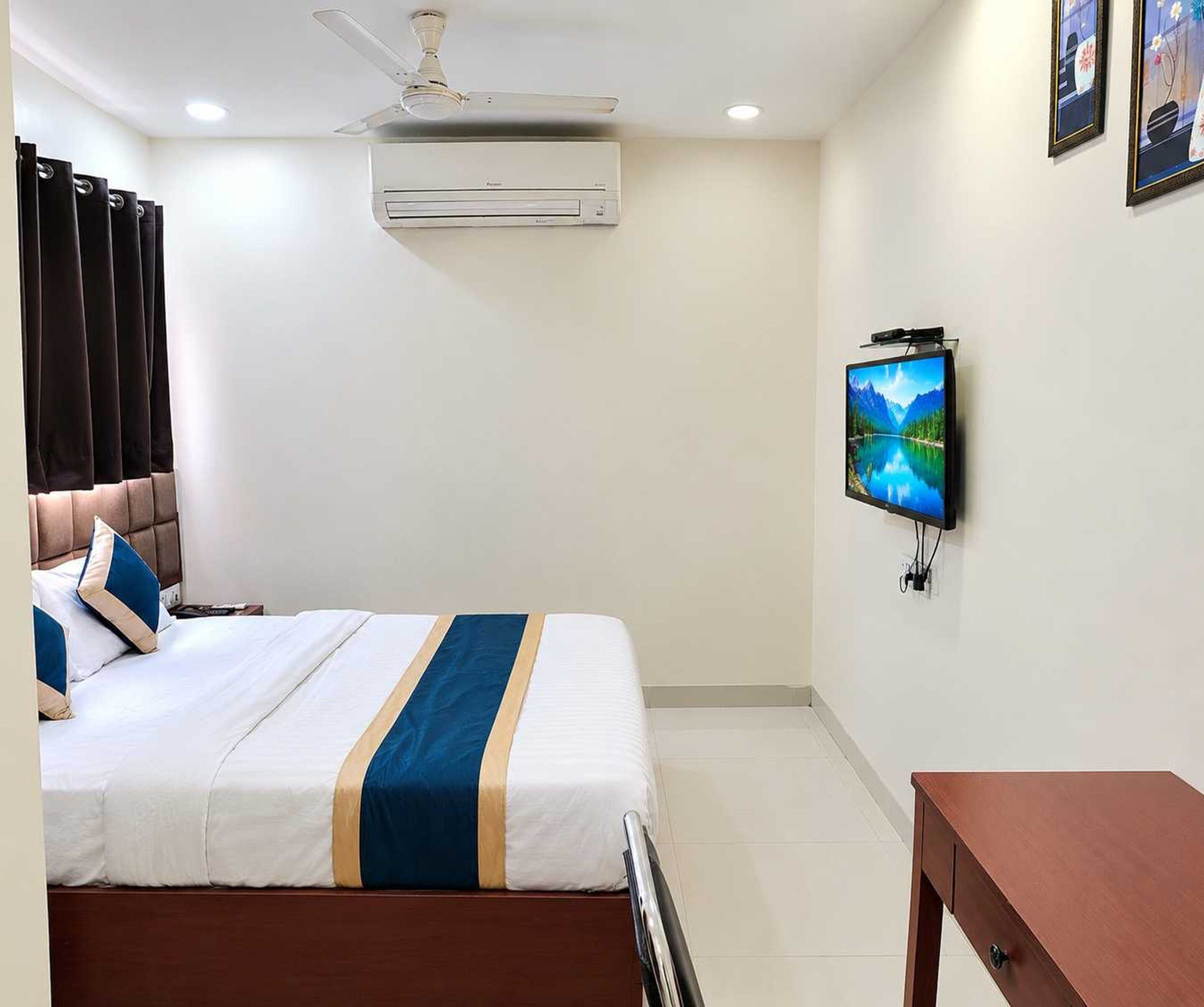 A hotel room with a bed, a television mounted on the wall, an air conditioning unit, and a ceiling fan.