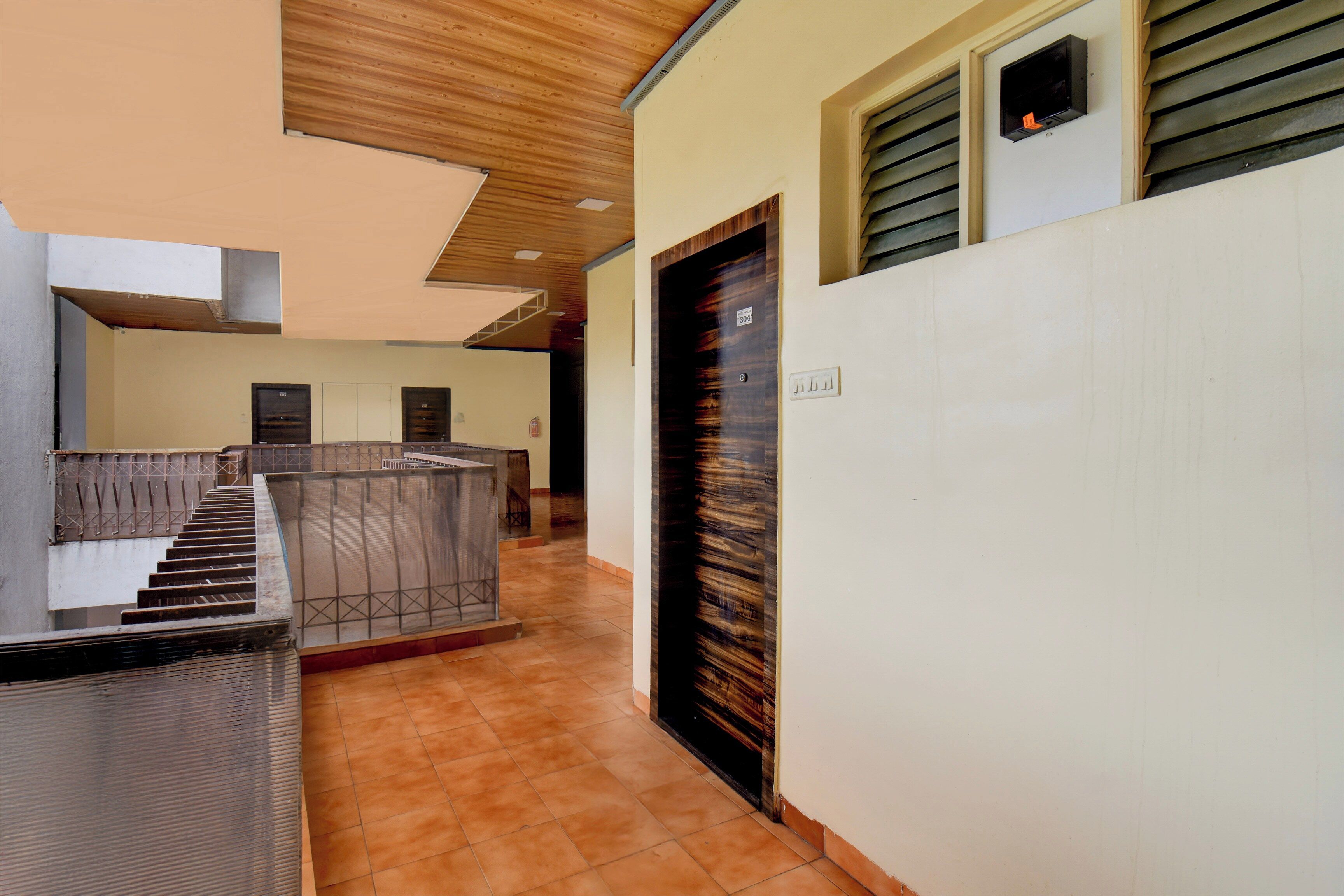 Pasillo de hotel con una escalera, una recepción y una puerta con placa de número.