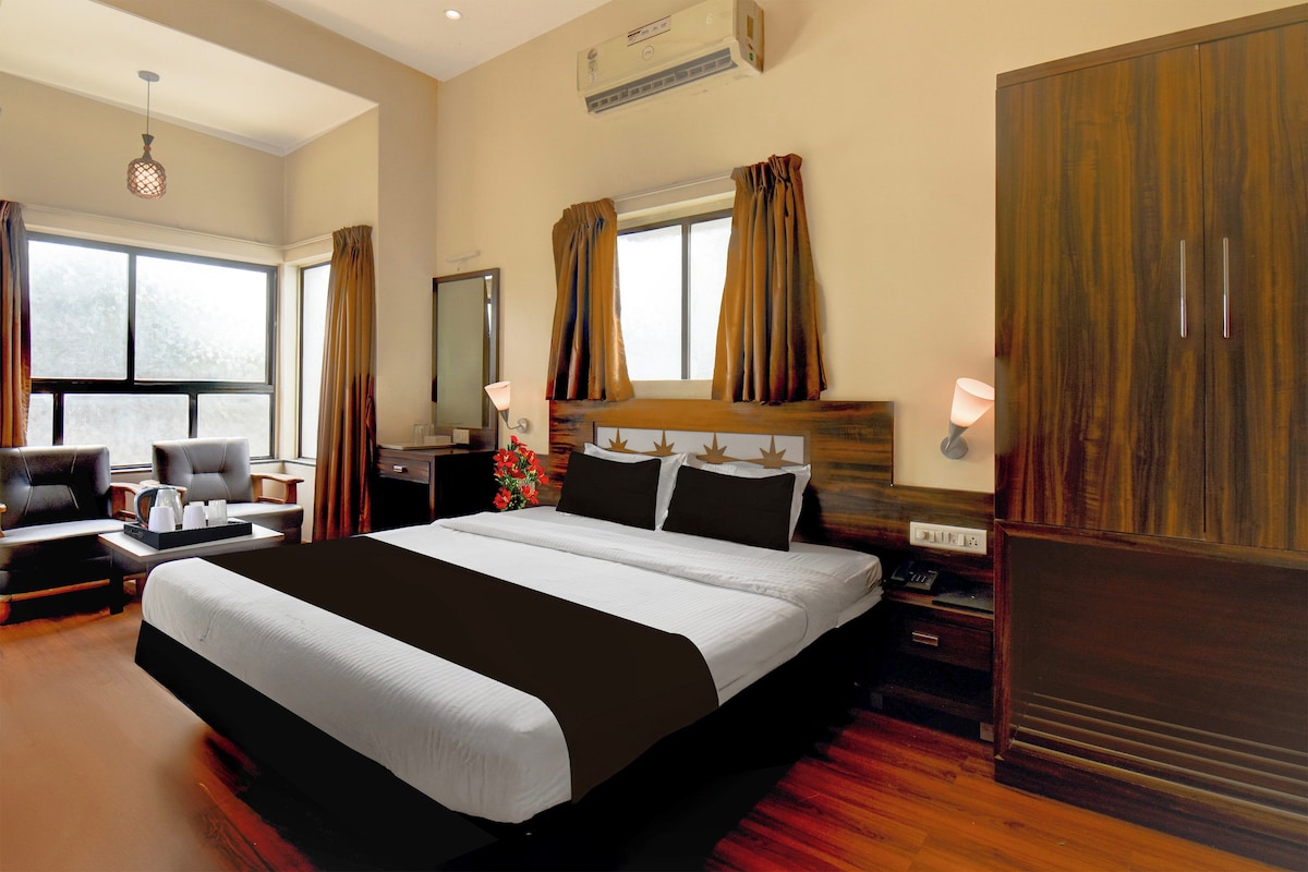 Habitación de hotel con una cama grande, un escritorio con silla, una ventana con cortinas y un armario de madera.