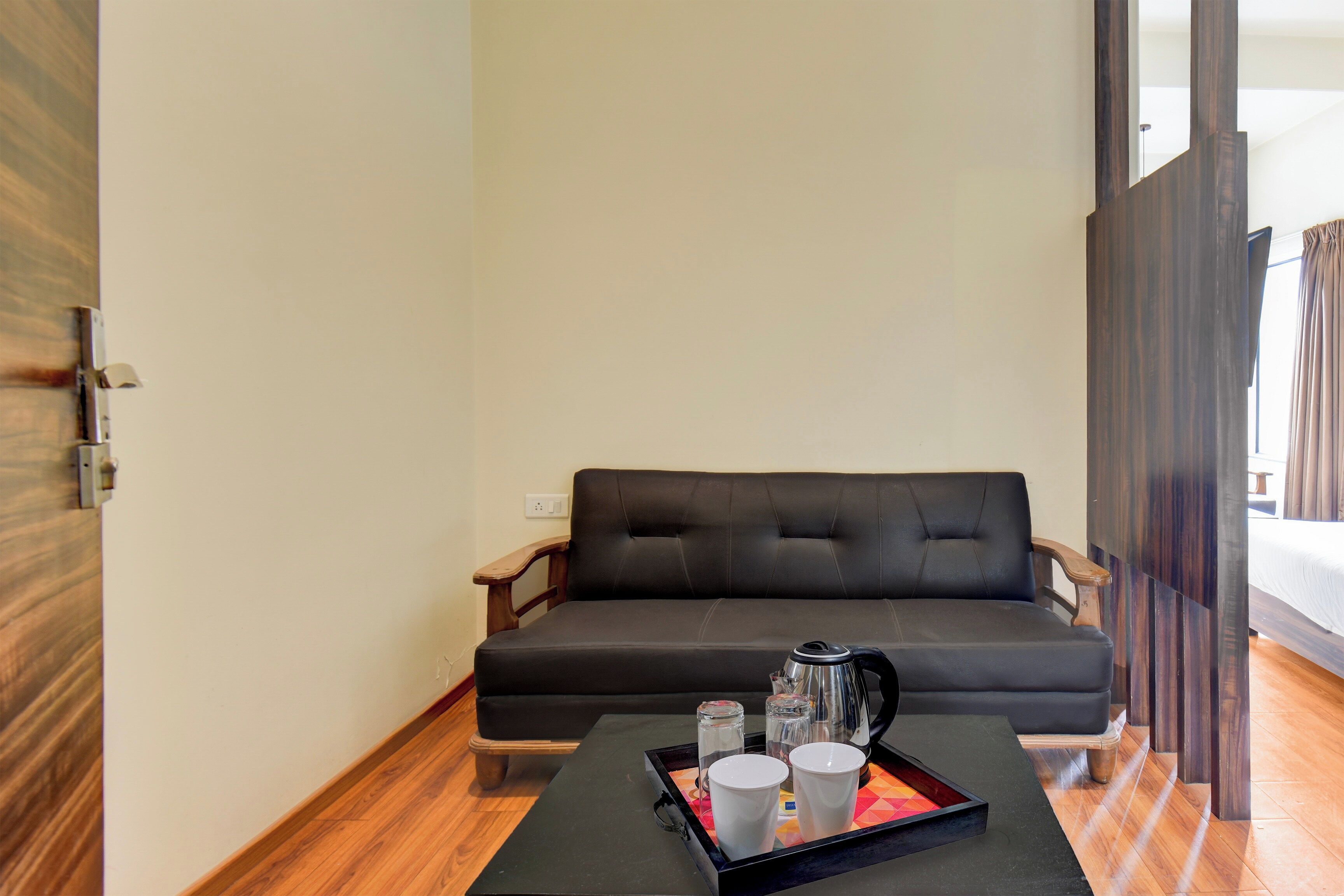 A modern room with a dark sofa, wooden floor, and a tray with cups and a kettle.