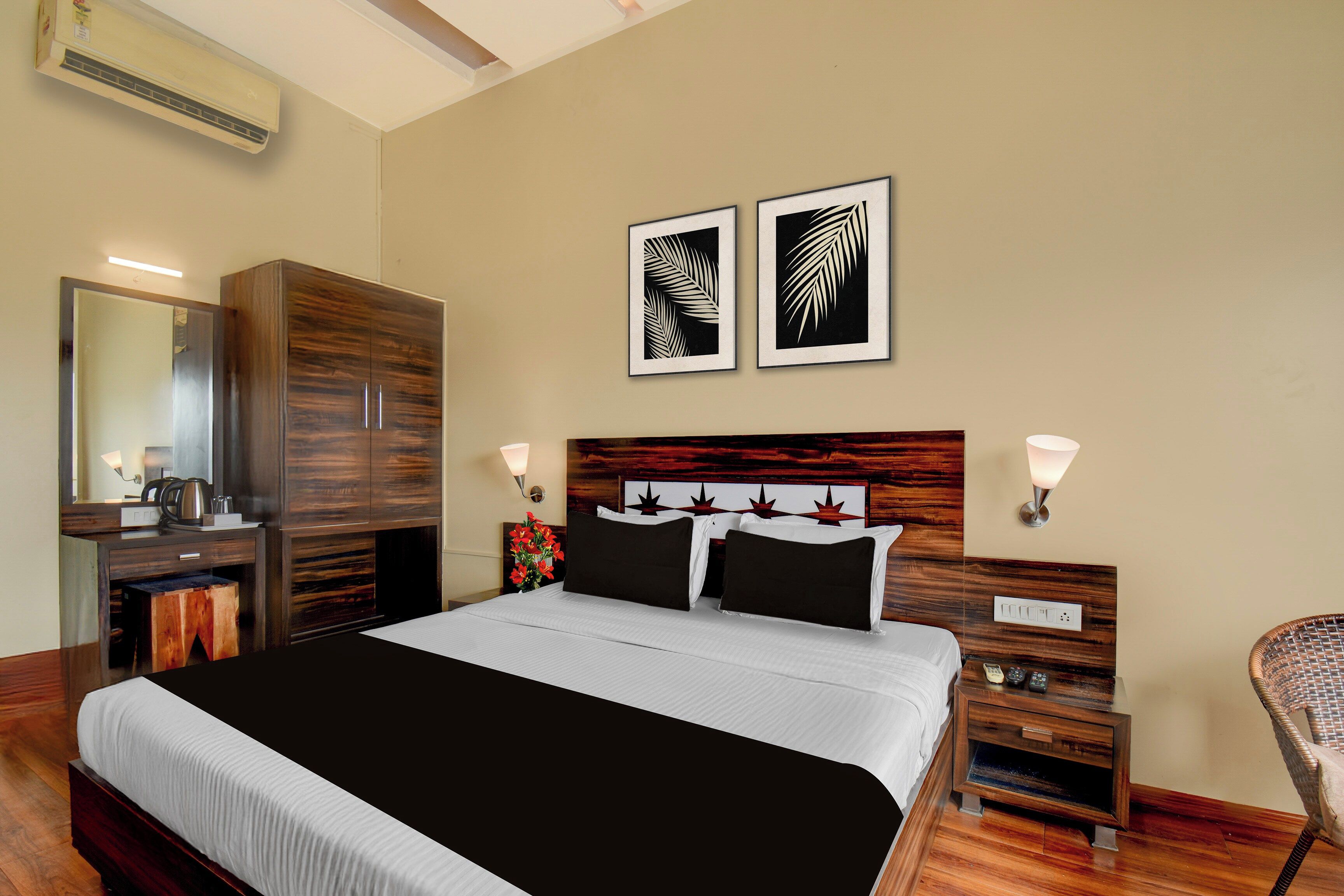 Una habitación de hotel con una cama grande, un armario, una mesita de noche con una lámpara y dos cuadros enmarcados en la pared.
