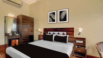 Una habitación de hotel con una cama grande, un armario, una mesita de noche con una lámpara y dos cuadros enmarcados en la pared.