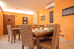 Un comedor con mesa de madera y sillas tejidas, aire acondicionado de pared y cuadros enmarcados.
