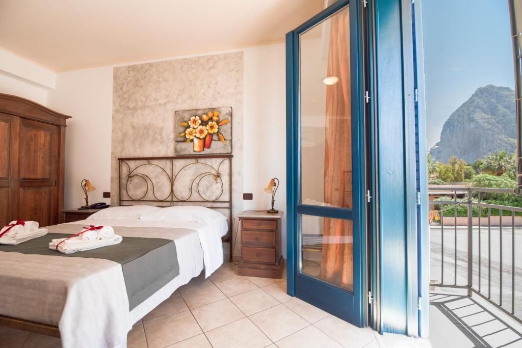 Habitación de hotel con cama, mesita de noche, un cuadro y balcón con vista a la montaña.