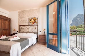 Habitación de hotel con cama, mesita de noche, un cuadro y balcón con vista a la montaña.