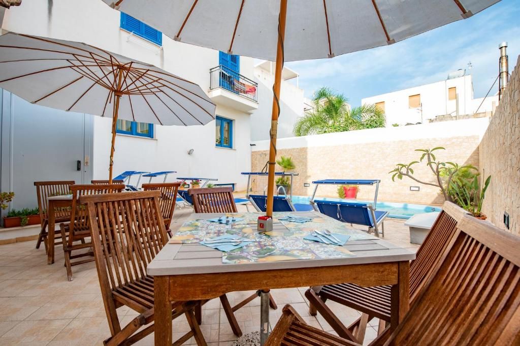 En udendørs patio med spisebord, stole, parasoller og en swimmingpool.