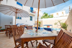 Un patio exterior con mesa, sillas, sombrillas y piscina.