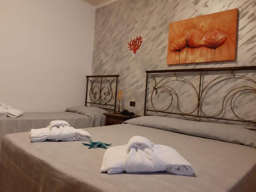 Et hotelværelse med to senge, hver med et pænt foldet håndklæde. Et billede hænger på væggen over sengene, og et lille bord med en lampe står ved den ene seng.