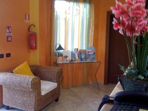 Vestíbulo de hotel con un sofá, una mesita con libros, un extintor y una planta en maceta.