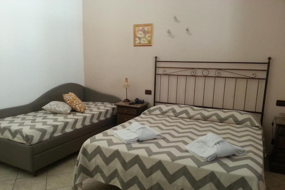Habitación con dos camas, cada una con colcha estampada, una mesita de noche con lámpara y un cuadro en la pared.