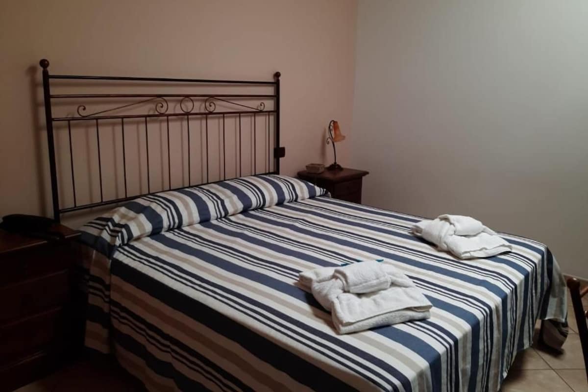 Una cama individual con una colcha a rayas, una mesita de noche con una lámpara y un par de toallas.