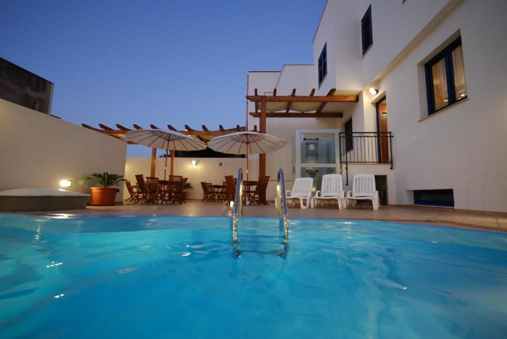 Una piscina con una pérgola y sombrillas, rodeada de mobiliario exterior y un edificio.