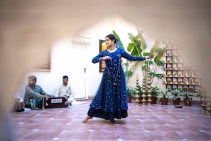 A person in a blue dress performing in a courtyard with tiled flooring, surrounded by potted plants and a decorative wall. - Justa Luxe Kashi Parampara, Varanasi (Varanasi)