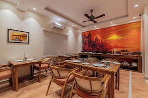 A dining area with multiple tables and chairs, an air conditioning unit, and a ceiling fan. - Justa Luxe Kashi Parampara, Varanasi (Varanasi)
