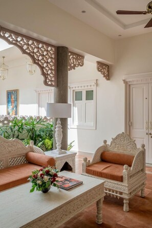 A room with a white sofa, a coffee table with a book and flowers, and a decorative pillar. - Justa Luxe Kashi Parampara, Varanasi (Varanasi)